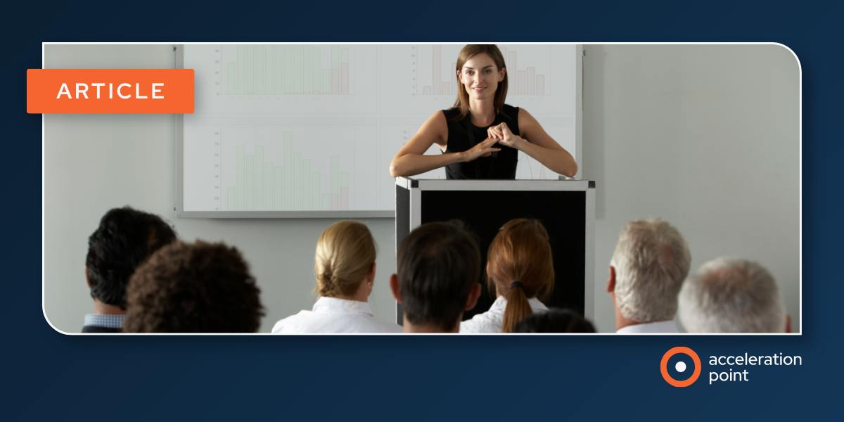 A presenter addresses a seated audience beside screens of data charts, reflecting the operational rigor behind an effective HCP contracting process.